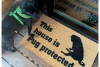 Lifestyle photo of black pug with doormat "This house is Pug protected"