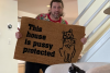 photo of a man showing a doormat reading This house is Pussy protected toa cat