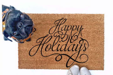 outdoor doormat reading happy holidays in script writing with a black pug puppy