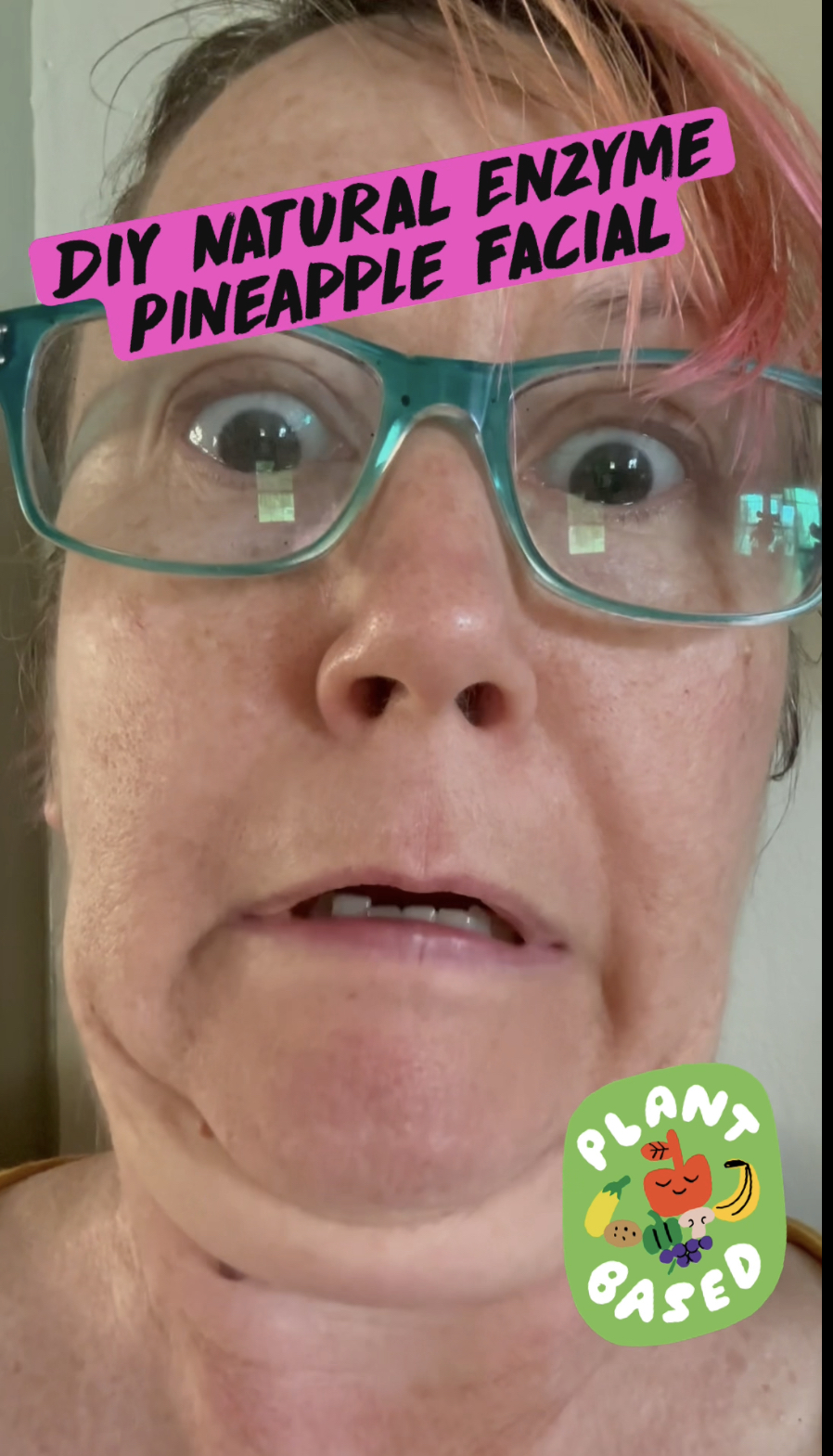 pink haired woman using fresh pineapple as a facial enzyme scrub making a funny face