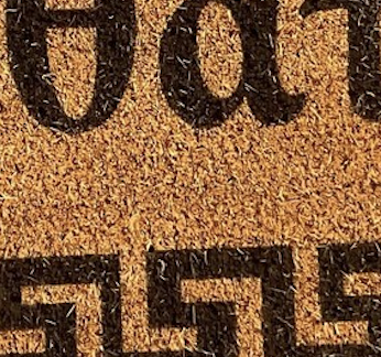 Close-up of Greek lettering reading Kalos Irthate on a natural coir doormat.