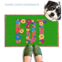 A terrier dog standing on a green doormat with the word "FDT" written on it, with a person's feet visible underneath.