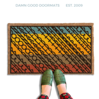 A pair of feet wearing green shoes stands on a subtle southwest style colorful, patterned FDT Fuck Donald Trump doormat