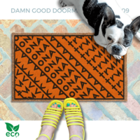 subtle fuck donald trump doormat in abstract contemporary design over a pumpkin orange fall doormat. A pair of feet wearing yellow strappy sandals with a french bulldog sitting on the floor next to them. 