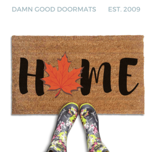 Coir doormat printed with HOME in black brush lettering, with an orange-red maple leaf standing in for the O