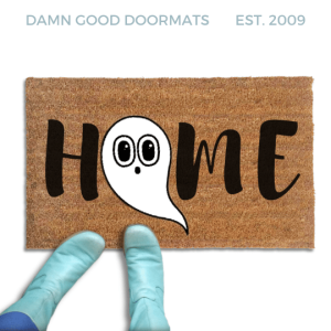 Coir doormat printed with HOME in black brush lettering, with a white cartoon ghost with big round eyes standing in for the O