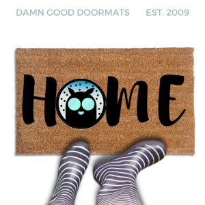 Coir doormat printed with HOME in black brush lettering, with Mothman's dark round silhouette and glowing teal eyes standing in for the O