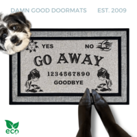a gray all weather welcome mat with a terrier dog, the word "GO AWAY" on it. The mat has a Ouija board design and the numbers "1234656789" printed on it. The scene includes a person's feet wearing black pointy toed witch boots and the text "DAMN GOOD DOORMATS EST. 2009" is visible.