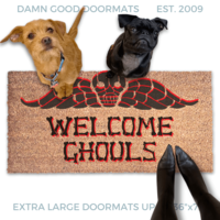 a terrier and a black pug dog sitting on a door mat with the text "WELCOME GHOULS" and a spooky Beetlejuice tombstone on it.