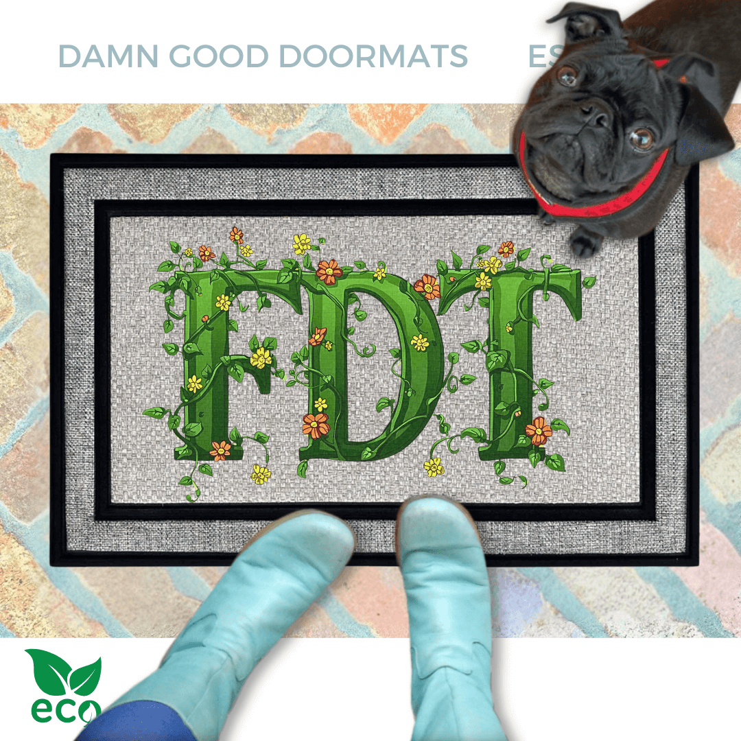 A dog standing on an all weather doormat with the word "FDT" written on it in green vines, with a person's feet visible underneath.