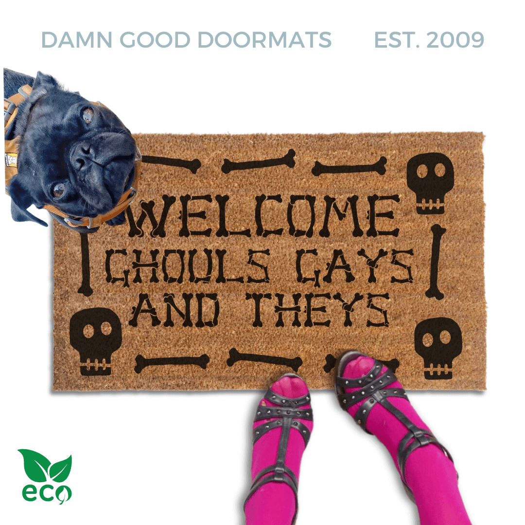 a humorous LGBTQ Halloween door mat with the text "Welcome Ghouls, Gays and Theys". There is also a pug and a person's feet visible in the image.