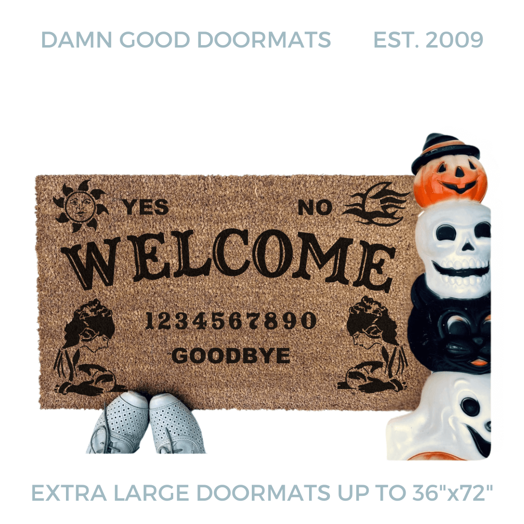 a welcome mat with the word "WELCOME" on it. The mat has a Ouija board design and the numbers "1234656789" printed on it. The scene includes a person's feet wearing white shoes, a vintage Halloween skull and cat light, and the text "DAMN GOOD DOORMATS EST. 2009" is visible.