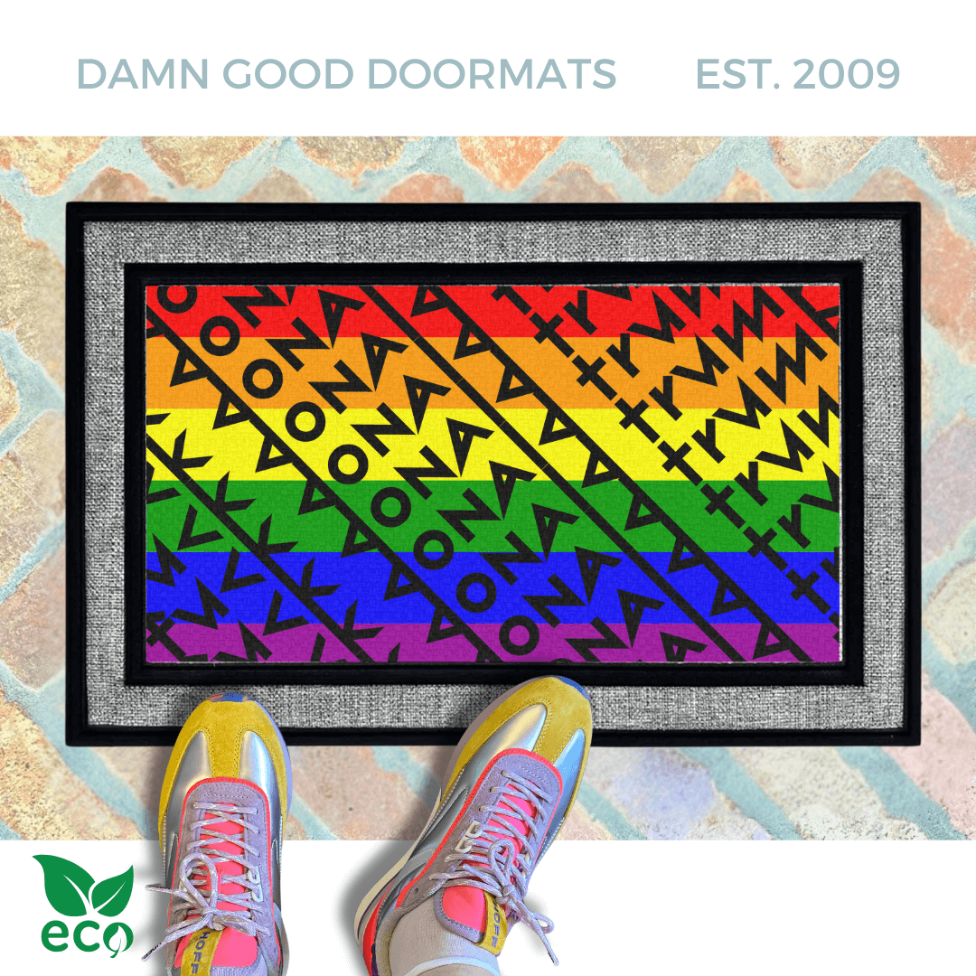 a pair of feet in colorful sneakers standing on a colorful gay pride rainbow flag doormat with a geometric Fuck Donald Trump pattern