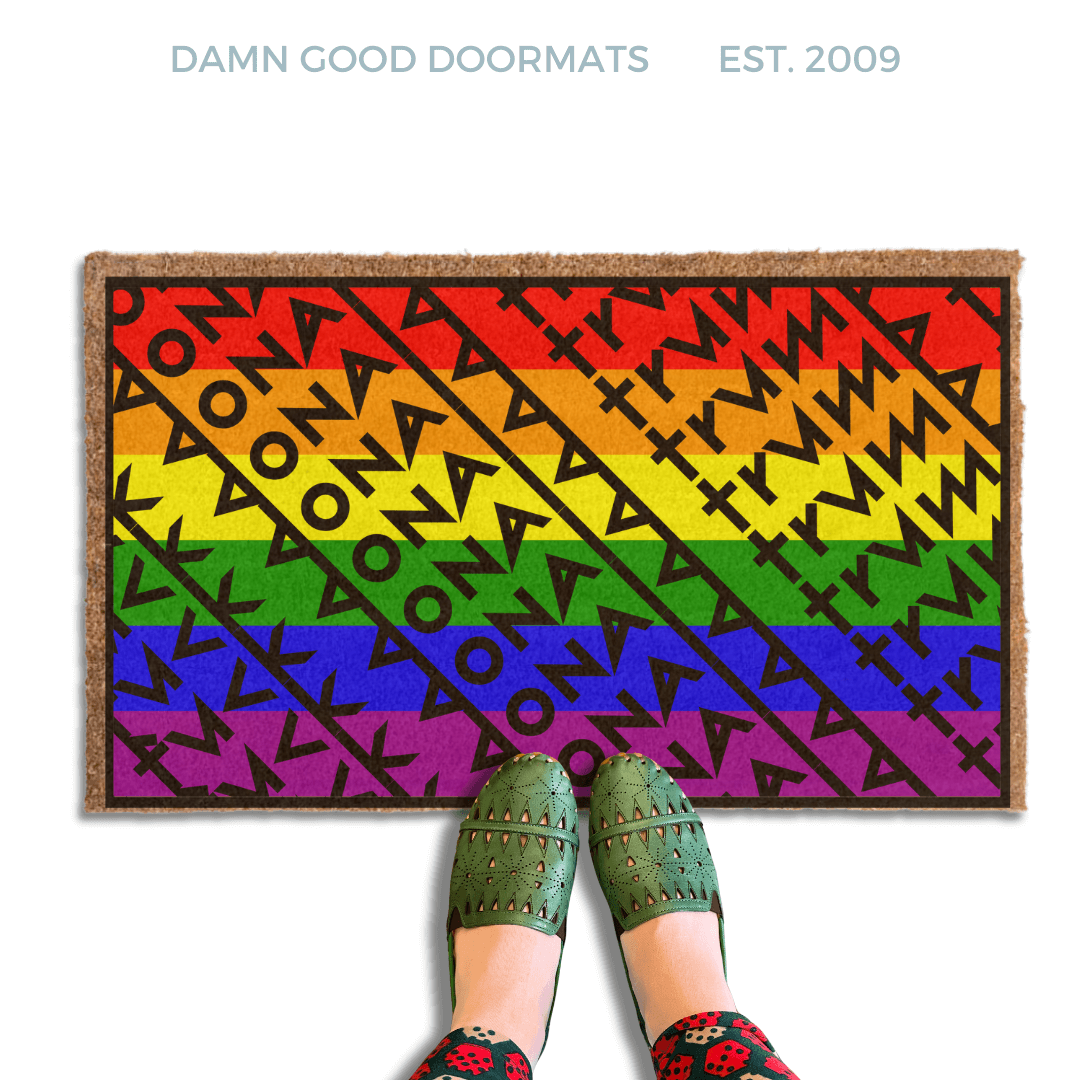 a pair of feet in green shoes standing on a colorful gay pride rainbow flag, patterned doormat with a geometric Fuck Donald Trump design .