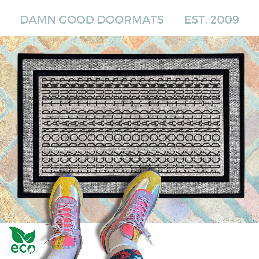 A pair of feet wearing green shoes stands on a subtle patterned FDT Fuck Donald Trump all weather doormat