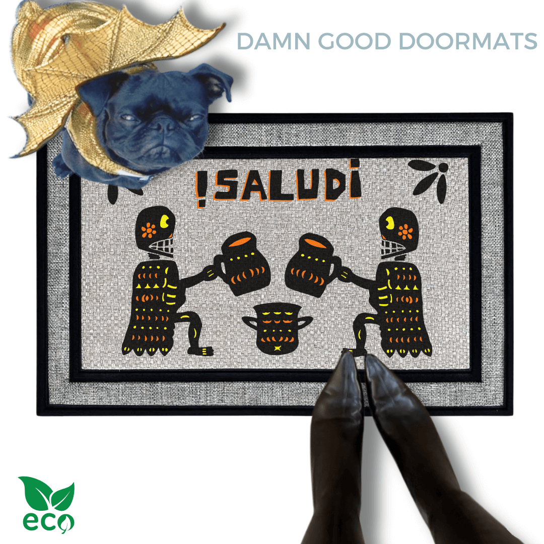 a pug in a gold dragon Halloween costume on a door mat with a Mexican Day of the Dead Halloween-themed design, including two skeletons, a pumpkin, and the text "¡Salud!"