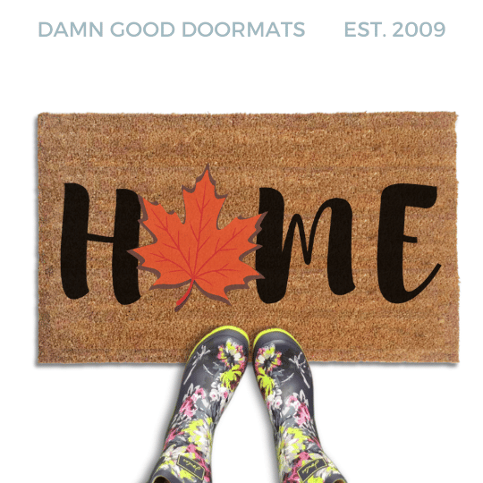 Coir doormat printed with HOME in black brush lettering, with an orange-red maple leaf standing in for the O