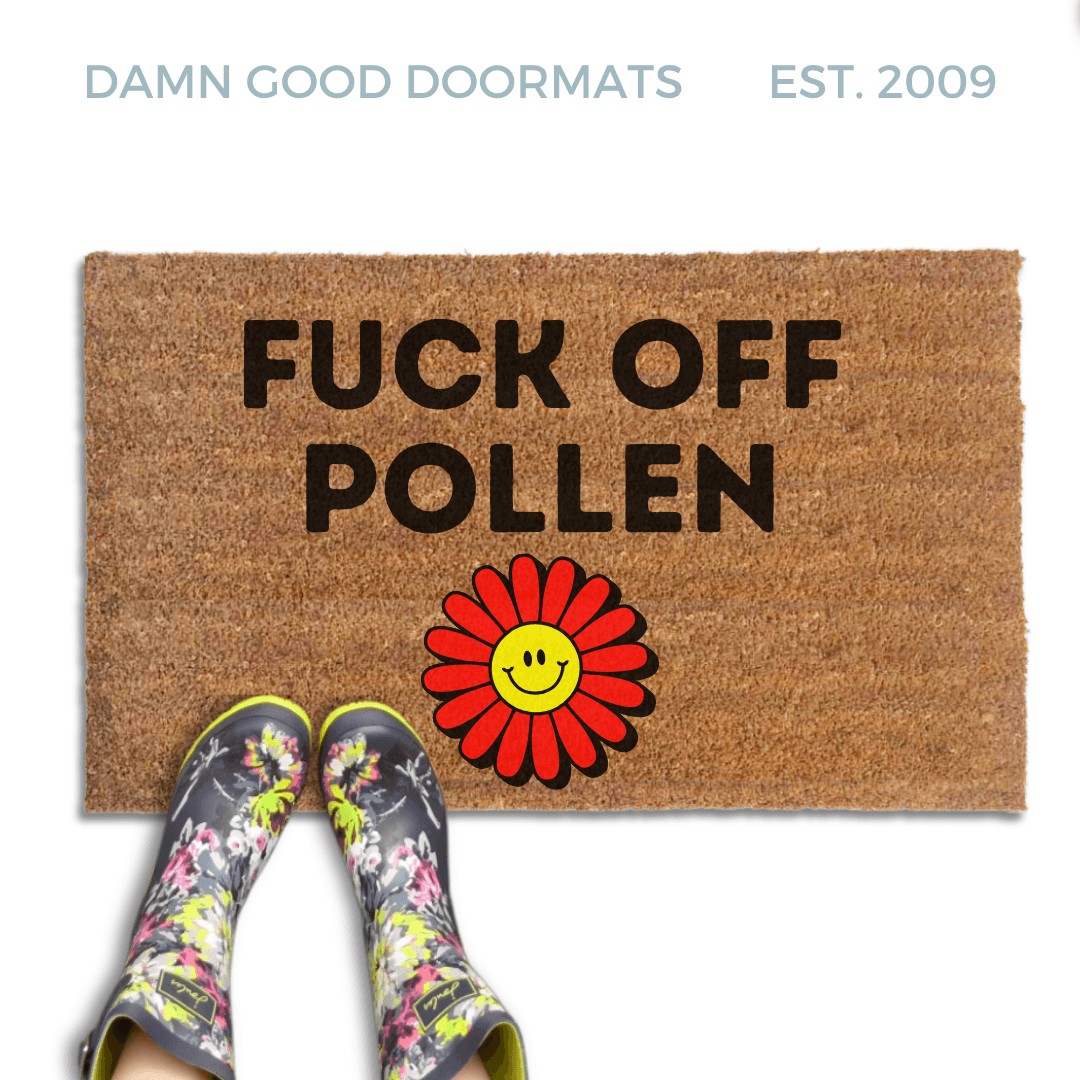 promotional image of a coir doormat reading "fuck off pollen" in with a red and yellow 70's hippy smiley faced flower on the bottom. A person in floral rain boots stands on the doormat