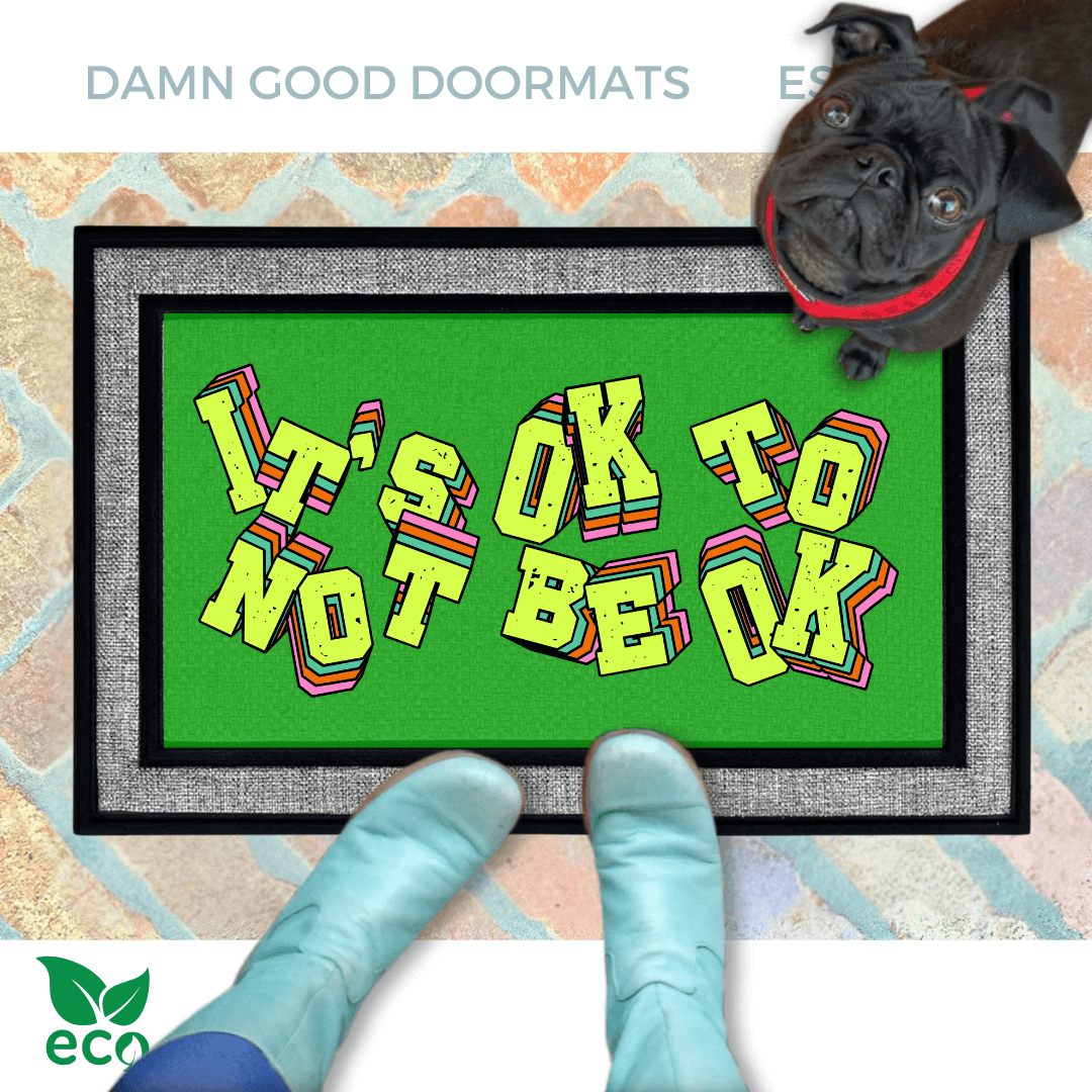 A pair of smurfy blue boots and a black pug dog are featured on a green doormat with the text "It's OK to BE OK" written on it.