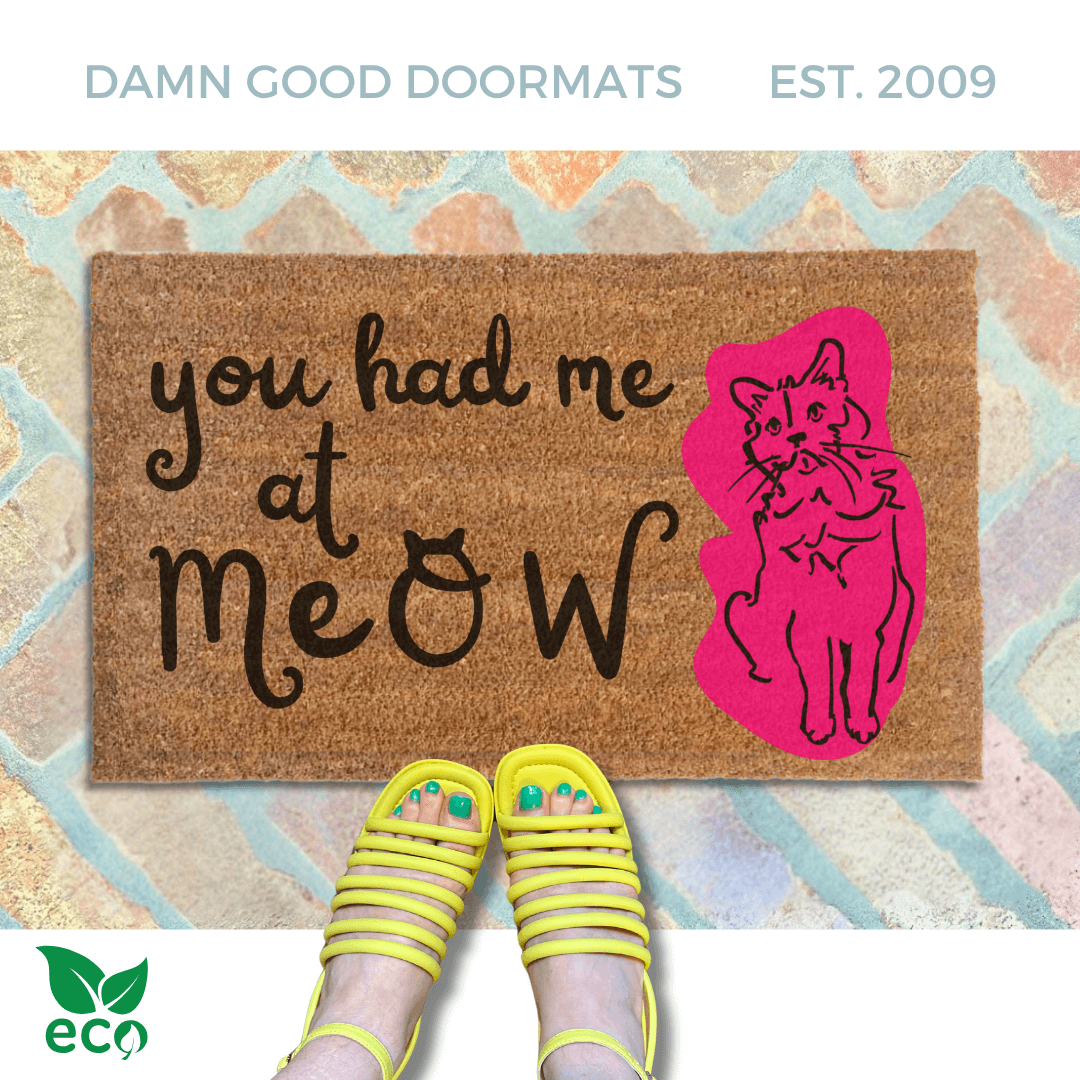 a pair of yellow strappy sandals on a brick floor, with a funny doormat. The text on the welcome mat reads "you had me at meow".