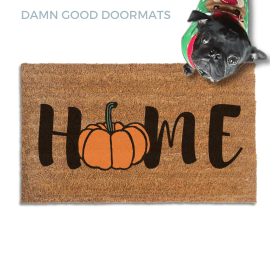 Coir doormat printed with HOME in black brush lettering, with an orange pumpkin standing in for the O