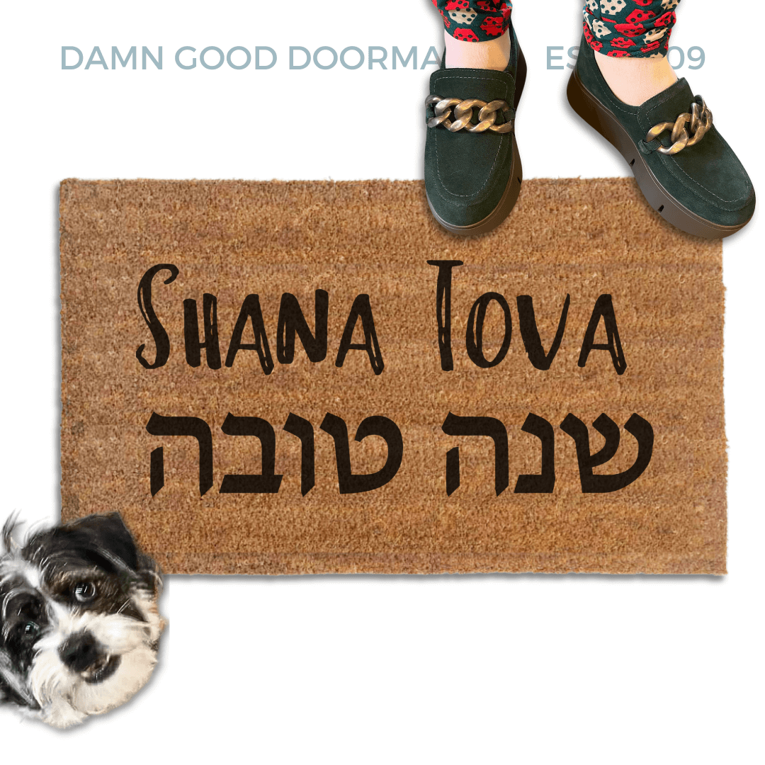 coir doormat reading Shana Tova in english and hebrew with a person in green shoes and a rescue terrier dog