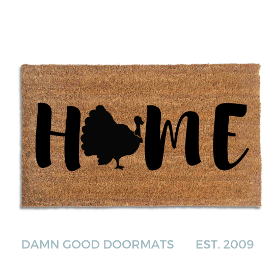 Coir doormat printed with HOME in black brush lettering, with a black turkey silhouette with a fanned tail standing in for the O