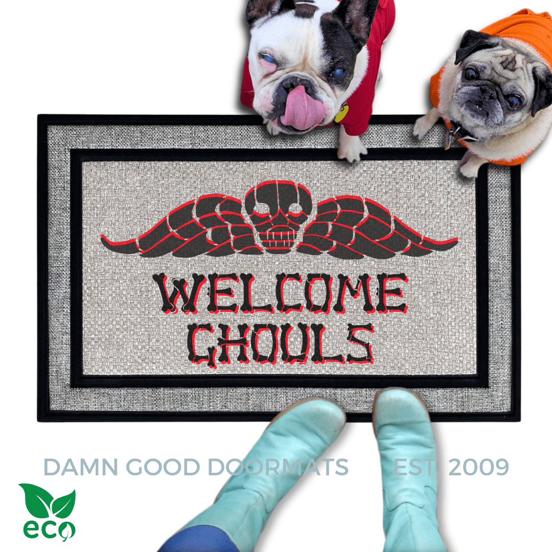 a french bulldog and a fawn pug dog in hoodies sitting on a door mat with the text "WELCOME GHOULS" and a spooky Beetlejuice tombstone on it.