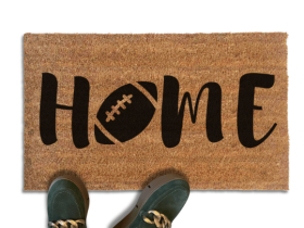 Coir doormat printed with HOME in black brush lettering, with a dark brown football with white laces standing in for the O