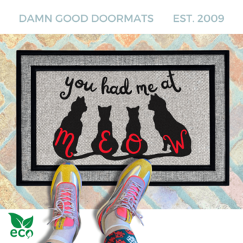 A pair of colorful sneakers stands on an all weather gray and black doormat with the text "you had me at meow" and silhouettes of cats