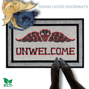 a small black pug in a gold dragon Halloween custom sitting on a welcome mat with the word "UNWELCOME" written on it in bones lettering
