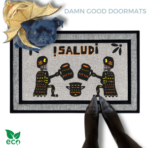 a pug in a gold dragon Halloween costume on a door mat with a Mexican Day of the Dead Halloween-themed design, including two skeletons, a pumpkin, and the text "¡Salud!"