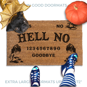 a Halloween welcome mat with a pug in golden dragon wings costume, the word "HELL NO" on it. The mat has a Ouija board design and the numbers "1234656789 GOODBYE" printed on it. The scene includes a person's feet wearing black pointy toed witch boots, an orange pupkin, and the text "DAMN GOOD DOORMATS EST. 2009" is visible.