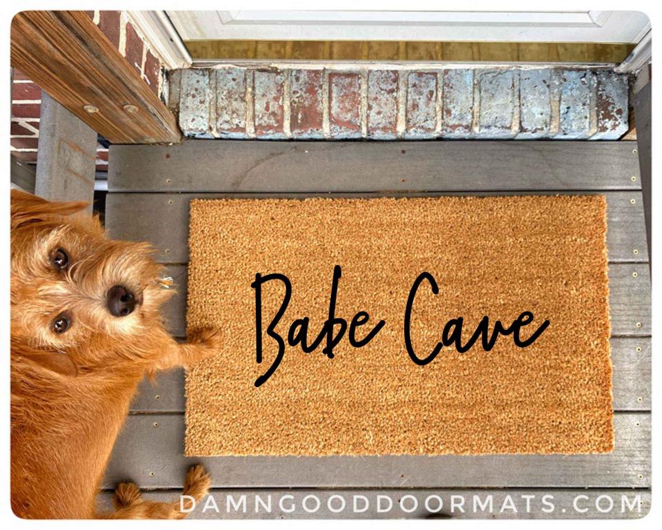 photo of an outdoor coir doormat reading "Babe Cave" with a red rescue terrier d