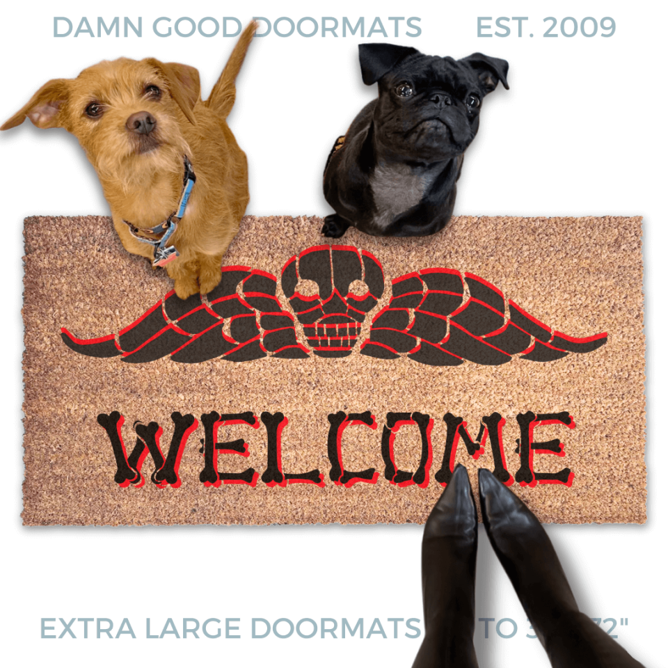 a dog and a small black pug and a terrier sitting on a welcome mat with a Beetlejuice skull design. The mat has the word "WELCOME" written on it in bones lettering