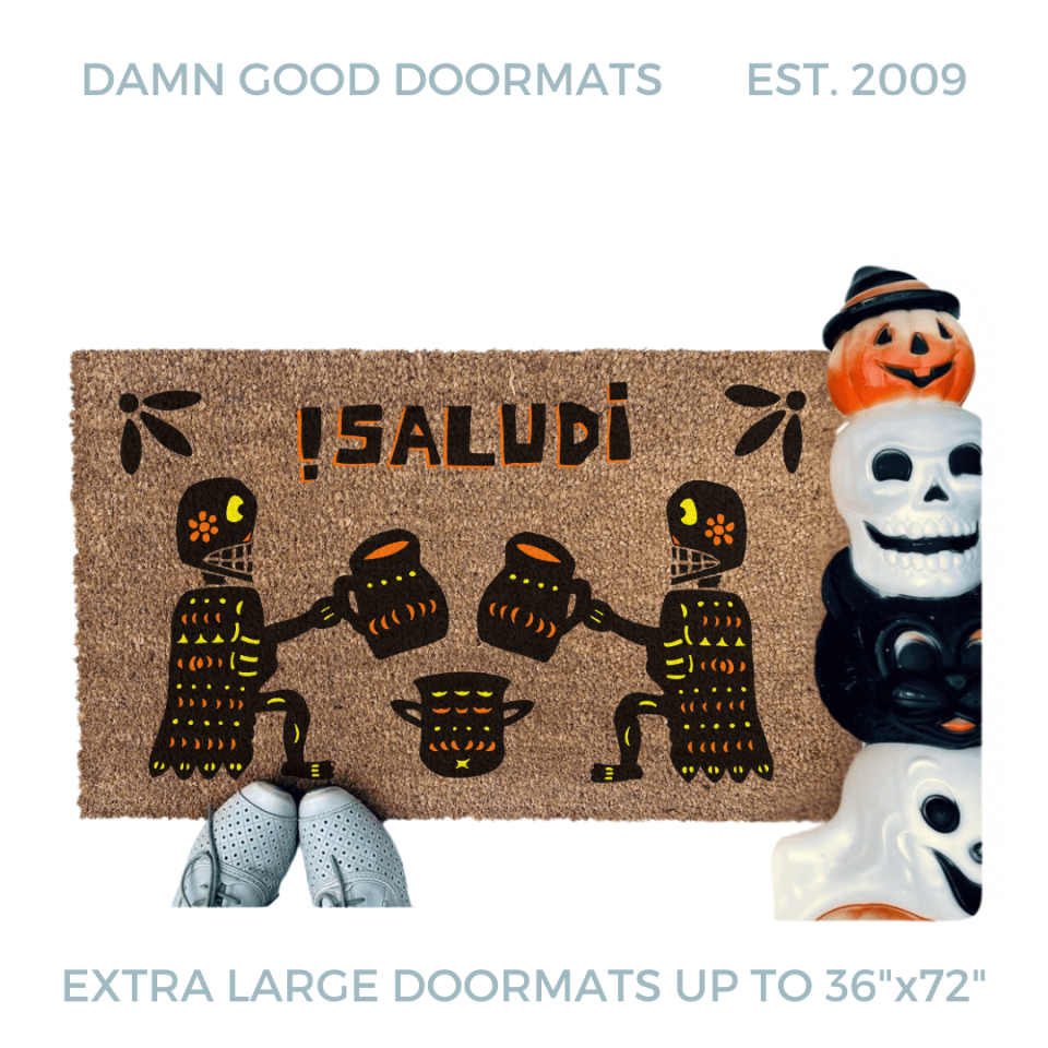 a door mat with a Mexican Day of the Dead Halloween-themed design, including two skeletons, a pumpkin, and the text "¡Salud!"