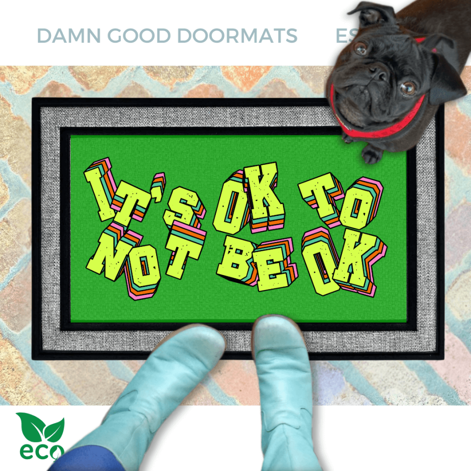 A pair of smurfy blue boots and a black pug dog are featured on a green doormat with the text "It's OK to BE OK" written on it.