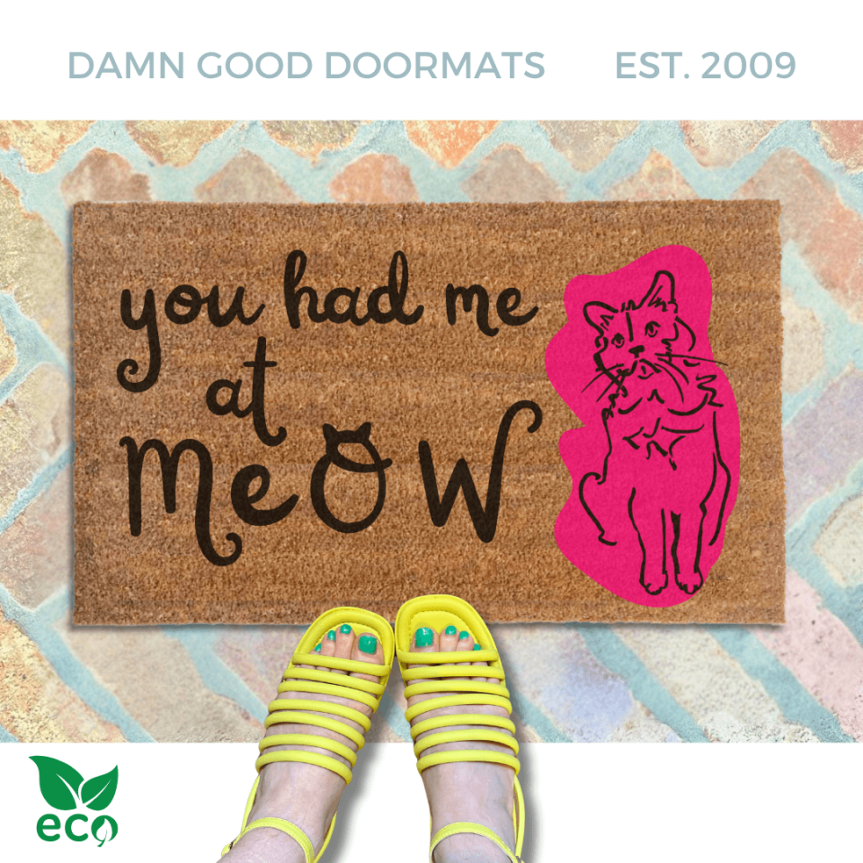 a pair of yellow strappy sandals on a brick floor, with a funny doormat. The text on the welcome mat reads "you had me at meow".