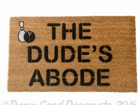 Natural tan coir doormat printed with The Dude's Abode in black bowling-style lettering — Big Lebowski welcome mat