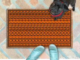 subtle fuck donald trump doormat in abstract contemporary design over a pumpkin orange fall doormat. A pair of feet wearing baby blue boots stands with a black pug dog sitting on the floor next to them. 