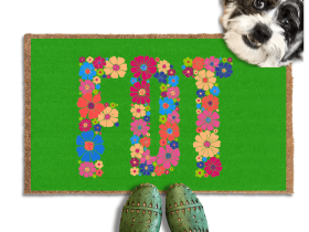 A terrier dog standing on a green doormat with the word "FDT" written on it, with a person's feet visible underneath.