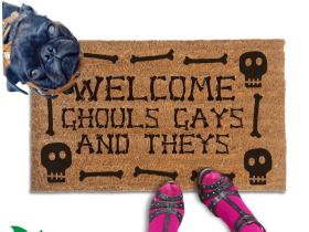 a humorous LGBTQ Halloween door mat with the text "Welcome Ghouls, Gays and Theys". There is also a pug and a person's feet visible in the image.