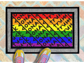 a pair of feet in colorful sneakers standing on a colorful gay pride rainbow flag doormat with a geometric Fuck Donald Trump pattern