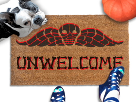 a french bulldog sitting on a welcome mat with the word "UNWELCOME" written on it in bones lettering