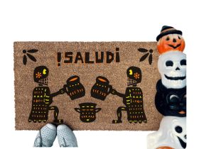 a door mat with a Mexican Day of the Dead Halloween-themed design, including two skeletons, a pumpkin, and the text "¡Salud!"