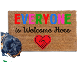 Everyone is welcome here doormat with a black pug standing on it looking up