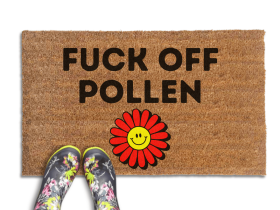 promotional image of a coir doormat reading "fuck off pollen" in with a red and yellow 70's hippy smiley faced flower on the bottom. A person in floral rain boots stands on the doormat