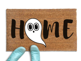 Coir doormat printed with HOME in black brush lettering, with a white cartoon ghost with big round eyes standing in for the O