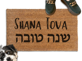 coir doormat reading Shana Tova in english and hebrew with a person in green shoes and a rescue terrier dog