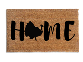 Coir doormat printed with HOME in black brush lettering, with a black turkey silhouette with a fanned tail standing in for the O